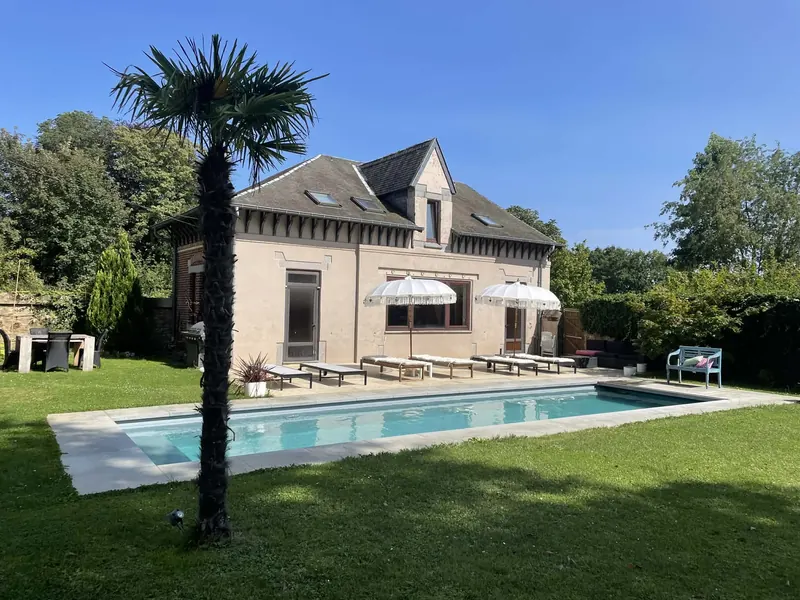The Villa O Poolhouse seen across its 12-metre heated pool, with a palm tree and sun loungers