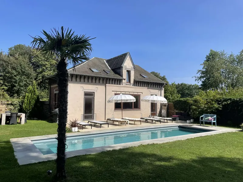 The poolhouse and palm tree beside the long heated pool on a sunny day